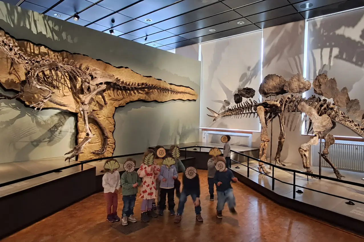 Kita-Gruppe im Museum, umrahmt von zwei riesigen Dinosaurier-Skeletten
